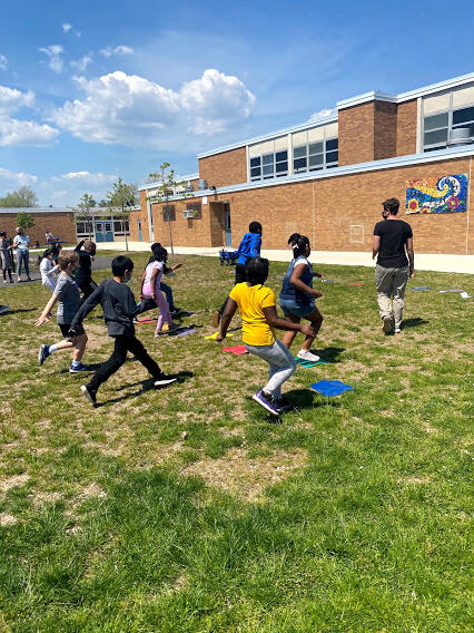 A large group of children running on a grassy area behind a school, playing a game.