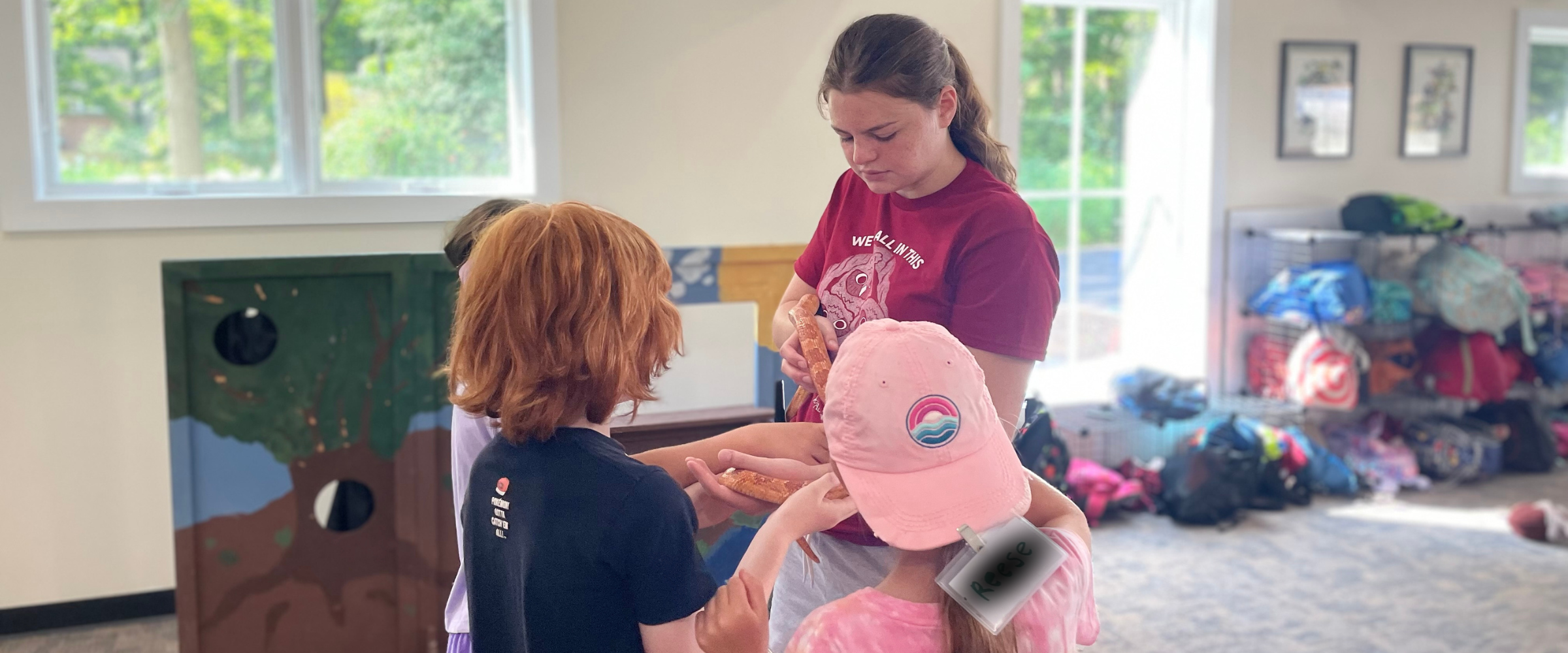 A camp counselor holds up a corn snake for a group of children to meet and observe.